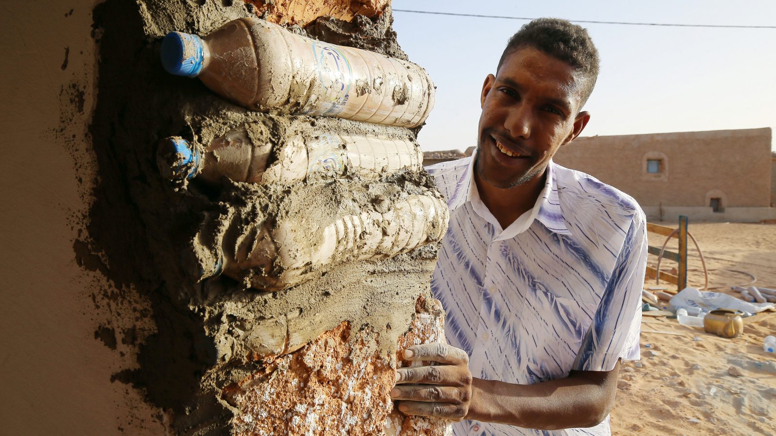 Tateh Lehbib montre comment construire une maison écologique à partir de bouteilles en plastique usagées remplies de sable. Les maisons circulaires construites dans le camp de réfugiés de Tindouf résistent au vent et aux fortes pluies et permettent de se protéger efficacement du rude climat qui caractérise le désert algérien.